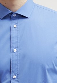 Světlomodrá košile na knoflíky z hladké látky s klasickým límcem a bílými knoflíky podél légy, s jednoduchým designem.