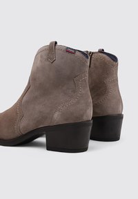 Bottines en daim marron avec un talon empilé. Présentent des coutures délicates et des languettes pour un enfilage facile. Texture douce avec une forme définie.