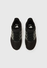 Fekete sportcipők fehér talppal, hálós felsőrésszel, fekete fűzőkkel és tépőzáras pánttal, egyszínű fehér háttér előtt, felülnézetből.