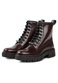 Botas de tobillo de cuero burdeos con un acabado brillante, que presentan un diseño de cordones negros, suelas de goma gruesa y detalles del logo en la parte frontal.