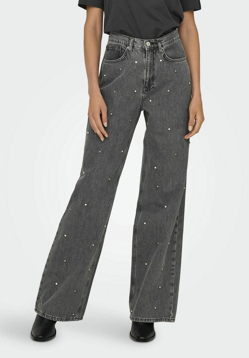 Pantalones vaqueros de mezclilla negra con piernas anchas, que presentan una cintura alta y pequeños adornos plateados esparcidos por toda la prenda. Bolsillos traseros lisos, diseño clásico.