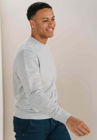 Grå bomuldssweatshirt med rund hals og lange ærmer, kombineret med mørkeblå bukser. Stoffet ser blødt ud med en subtil tekstur.