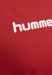 Roter Stoff mit glatter Textur, auf dem das Wort "hummel" in fettgedruckten, weißen Kleinbuchstaben schräg angeordnet ist.
