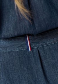 Džínová sukně s plisovaným designem, tmavě modré barvy a pasem zdobeným proužkovaným detailem v červené, bílé a modré barvě.