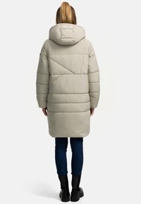 Lichtgrijze pufferjack met capuchon, met geometrische gestikte patronen, lange mouwen en een ontspannen pasvorm, gecombineerd met donkere jeans en laarzen.