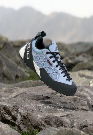 Lyseblå klatresko med svart gummisåle, sekskantmønster og svarte detaljer. Har lisser og en trekklapp på hælen.