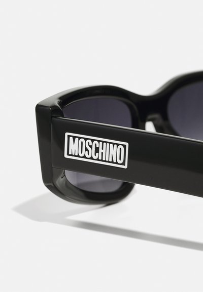 Črne sončna očala z velikimi okvirji. Imajo temno zaščitna leča in poudarjen bel logotip "Moschino" na ročaju. Gladek plastičen zaključek.