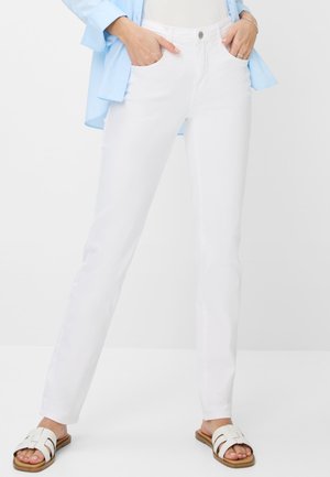 Weiße Jeans im geraden Schnitt mit vorderen Taschen. Kombiniert mit einem hellblauen Hemd und weißen Riemchensandalen auf flachen Sohlen.