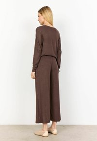 Bruine jumpsuit met lange mouwen en wijde benen, gemaakt van soepel materiaal, met een ruime pasvorm en een subtiele textuur, gecombineerd met lichte, geprinte ballerina's.