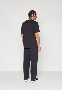 Sort kortærmet t-shirt og løse, mørke bukser. Materialet virker blødt; designet er simpelt. Skoene har hvide og sorte accenter.