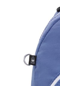 Mochila de tela azul con una superficie texturizada, que presenta un anillo plateado circular y una etiqueta negra con un detalle gráfico blanco.