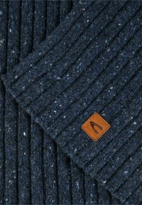 Strikket blå tørklæde med tekstureret ribmønster, med strejf af lysere blå og et rektangulært brunt lædermærke med logo.