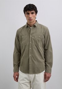 Chemise boutonnée vert olive en tissu doux, dotée de deux poches poitrine et d'un col classique. Manches longues avec poignets à boutons.