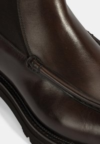 Bottine en cuir marron avec des panneaux latéraux élastiques, texture lisse, couture décorative et semelle en caoutchouc pour l'adhérence et la durabilité.