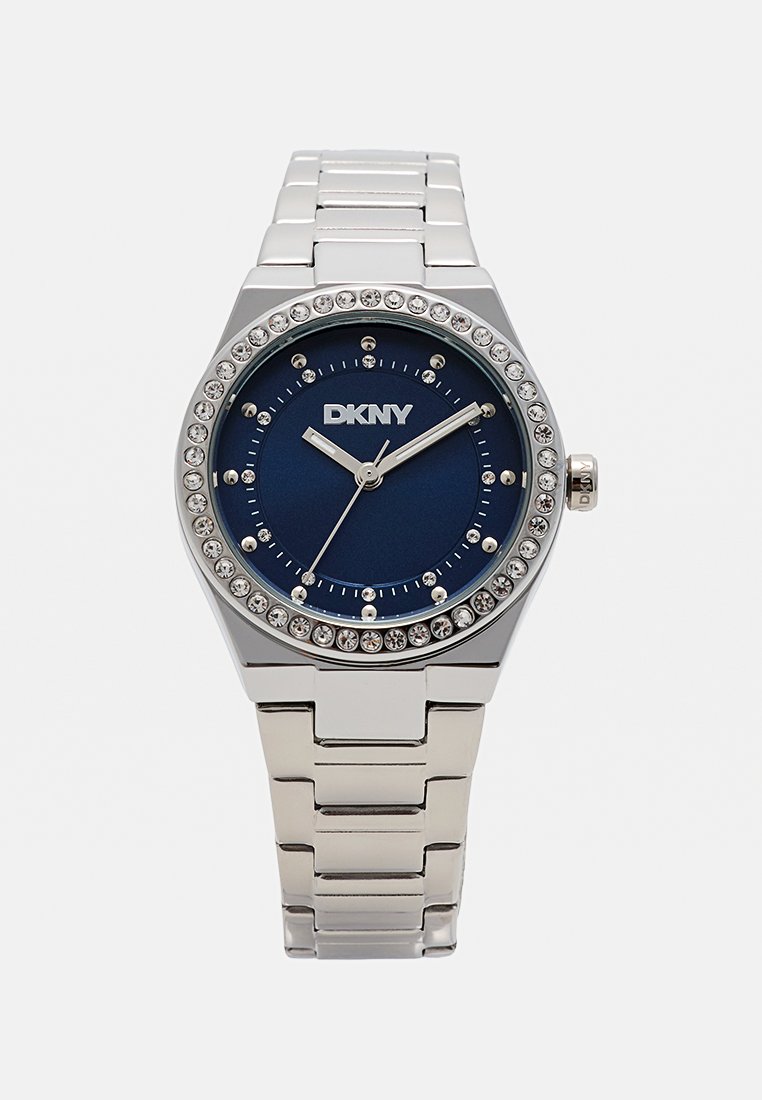 Orologio DKNY in tono argento con quadrante blu, dettagli in cristallo attorno alla lunetta e bracciale a maglie in metallo. Presenta indicatori e lancette semplici per le ore.