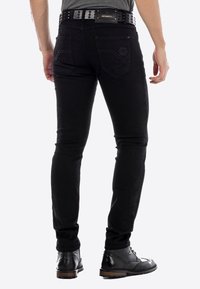 Zwarte denim jeans met een slim fit, vijf zakken ontwerp en subtiele stiksels. Een gestructureerde zwarte riem completeert de outfit.