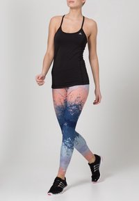 Débardeur de sport noir associé à des leggings multicolores avec un motif éclaboussé bleu et rose. Chaussures de sport noires avec des accents blancs.
