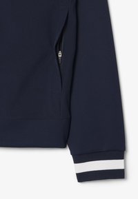 Sudadera azul marino con un bolsillo con cremallera y puños acanalados con rayas blancas. Tejido suave con un corte relajado y un diseño moderno.