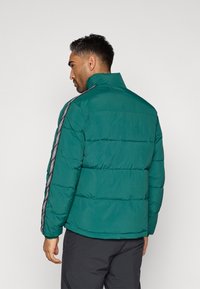 Τιρκουάζ μπουφάν πούλινγκ με στήριγμα για το λαιμό και οριζόντια ραφή, με μαύρες και λευκές πλευρικές ρίγες με σχέδιο. Παχύ, θερμομονωτικό υλικό.