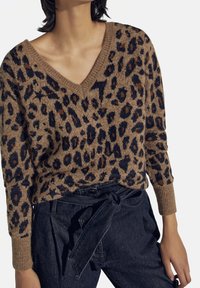 Brun och svart leopardmönstrad stickad tröja med V-ringning och ribbade ärmslut, bärs tillsammans med högmidjade, knutna mörka jeans.