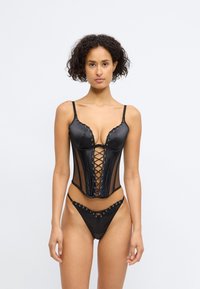 Corsé negro con cordones, con paneles de satén y malla, que presenta tirantes ajustables y un bikini a juego con detalles de ojales.