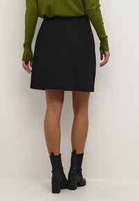 Black A-line skirt with a smooth texture and a waistband, paired with black ankle boots. The outfit features a green long-sleeve top.