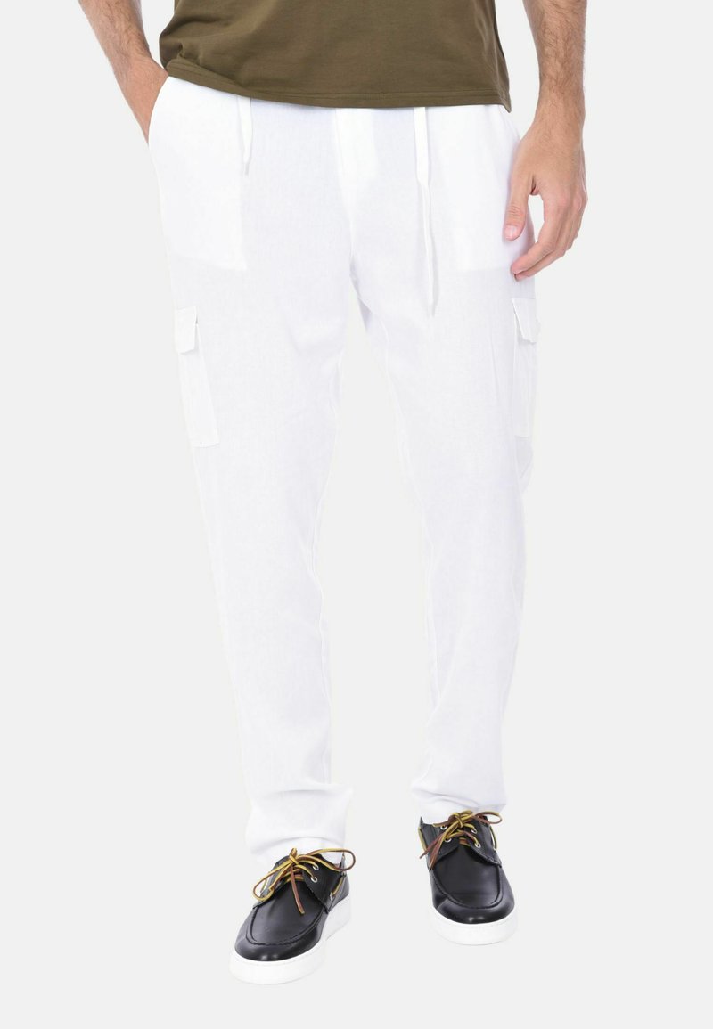 Pantaloni cargo bianchi con tasche laterali, vita con cordoncino e vestibilità rilassata, abbinati a scarpe nere con lacci gialli e suole bianche.