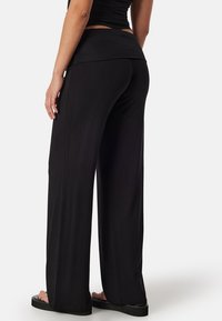 Zwarte wijde broek gemaakt van lichtgewicht stof met een aansluitende tailleband. Het ontwerp heeft een zachte textuur en een volledige lengte.