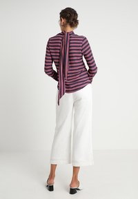 Blusa a maniche lunghe a righe blu navy con un fiocco sul retro, abbinata a pantaloni bianchi a gamba larga e mule nere con tacco. Tessuto dalla finitura liscia.