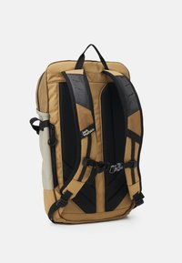 Brauner und beige Stoff-Rucksack mit Netzträgern, verstellbaren Schnallen und gepolstertem Rücken für Komfort. Mit Logo an der Seite.