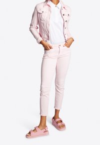 Chaqueta de mezclilla rosa claro y jeans ajustados a juego, combinados con sandalias rosas con tiras ajustables y suela gruesa. Blusa blanca simple debajo.