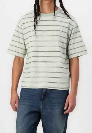 Gestreiftes Kurzarmhemd in Hellgrün und Weiß aus strukturiertem Stoff, kombiniert mit blauen Denim-Jeans. Verfügt über einen Rundhalsausschnitt.