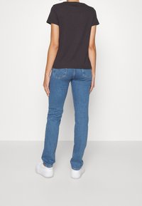 T-shirt nera di cotone a maniche corte, abbinata a jeans di denim blu con tasche posteriori, e sneakers bianche su uno sfondo chiaro.