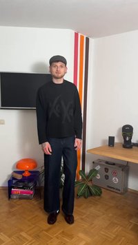 Schwarzes Langarmshirt mit Grafikdruck, kombiniert mit dunkelblauen Jeans mit weitem Bein und braunen Schuhen, vor einem minimalistischen Innenraumhintergrund.