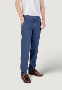 Chinos in cotone blu navy con vestibilità dritta, dotati di tasche laterali, chiusura con bottone e abbinati a scarpe da barca marroni.