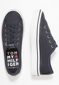 Marina canvas sneakers med vit gummisula, gyllene öglor och marina snören. Logotypen på insidan har en röd stjärna och varumärkesnamn.