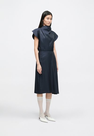 Temno modra obleka z visokim ovratnikom, kapnimi rokavi in A-linijo. Dopolnjena z belimi mule in prosojnimi nogavicami do gležnjev. Gladka tekstura.