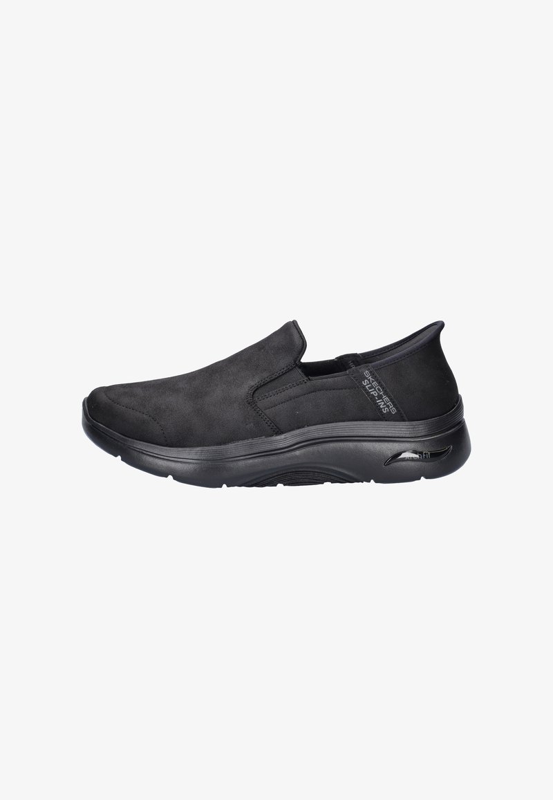 Zapatos negros sin cordones hechos de un material similar al ante con una textura suave, punta redonda y suela acolchada diseñada para la comodidad.