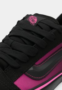 Nærbilde av sorte og rosa Vans-sko som viser snøring, logo på tungen og side stripe med detaljert søm.