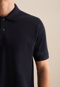 Granatowa koszulka polo z krótkim rękawem, teksturowany materiał, zapięcie na trzy guziki i klasyczny kołnierzyk.