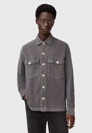 Grijze ribfluwelen jas met een kraag, twee voorzakken en contrasterende crèmekleurige knopen. Gelaagd materiaal met een gestructureerd ontwerp.