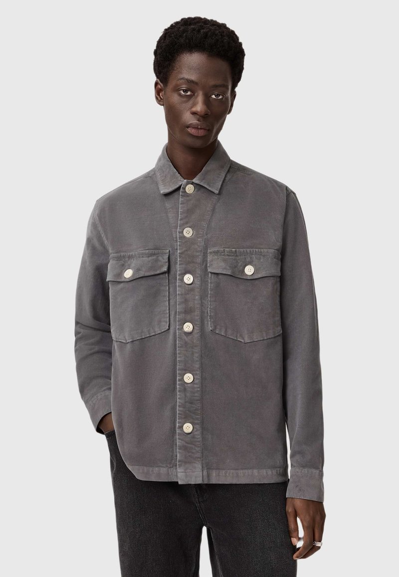 Grijze ribfluwelen jas met een kraag, twee voorzakken en contrasterende crèmekleurige knopen. Gelaagd materiaal met een gestructureerd ontwerp.