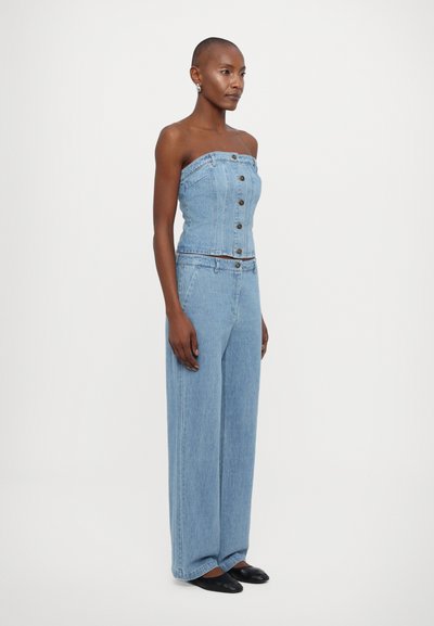 Uten skulderstropp denim jumpsuit i lys blå, med en tettsittende topp med knapper og vide bukser. Jevn tekstur og avslappet design.