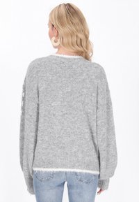 Grau gestrickter Pullover mit entspannter Passform, der eine weiche Textur und einen flauschigen weißen Saum hat. Knopfdetails an den Ärmeln.