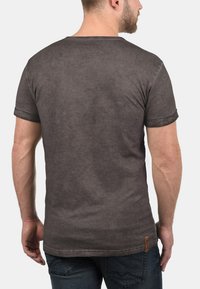 Grå kortærmet T-shirt med en let figursyet design og rullekanter. Blødt, struktureret stof med et lille broderet mærke ved kanten.