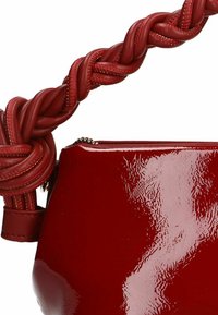 Red glossy handbag with a braided leather handle. Features a zip closure and smooth texture. The design emphasizes a rounded shape.