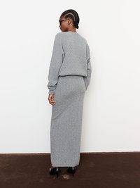 Szürke kötött pulóver és szoknya szett, struktúrált mintával, hosszú ujjakkal és testhez simuló szabással, fekete magassarkú cipővel párosítva.