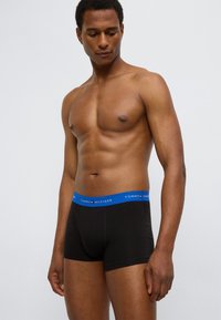 Μαύρα βαμβακερά μπόξερ με μπλε ελαστική μέση που φέρει το λογότυπο "TOMMY HILFIGER". Ο σχεδιασμός είναι εφαρμοστός και χωρίς ραφές.