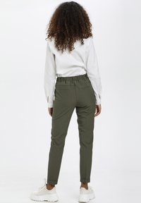Olive green tapered pants with an elastic waistband, two back pockets, and rolled hems, paired with a white long-sleeve shirt.