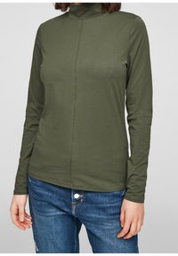 Langarm, olijfgroene coltrui met een zachte textuur en een verticale naad die over de voorkant loopt. In combinatie met blauwe jeans.